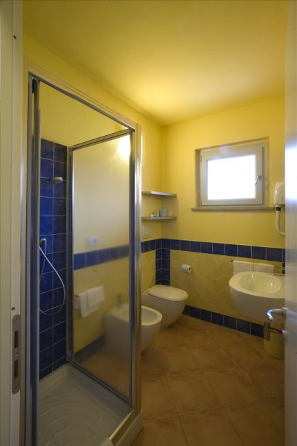 Bagno con doccia moderna, piastrelle blu, lavabo e wc, illuminato da una finestra.
