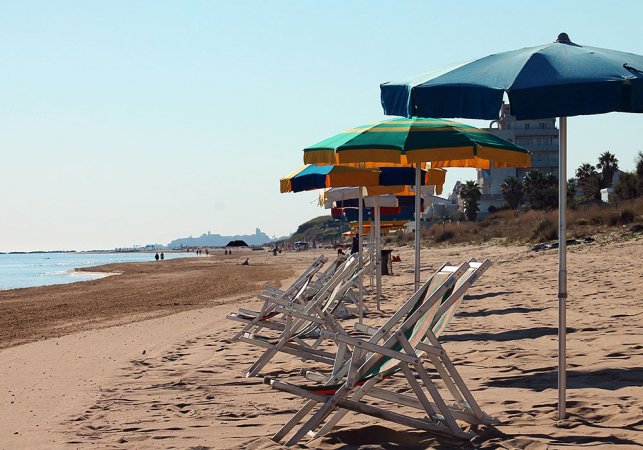 Spiaggia deserta con lettini e ombrelloni allineati.