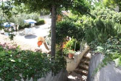 Scalinata tra piante rigogliose conduce a una terrazza con ombrelloni e tavoli all'aperto.