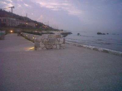 Lungomare al tramonto con scogliera e luci sul marciapiede.