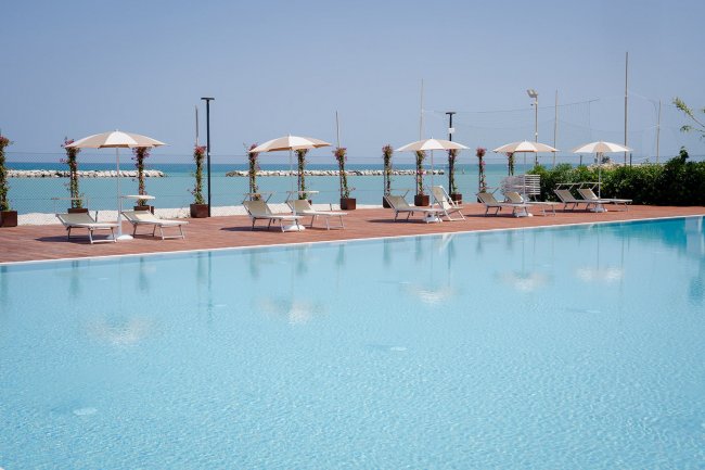 Piscina con ombrelloni e lettini, vista mare.