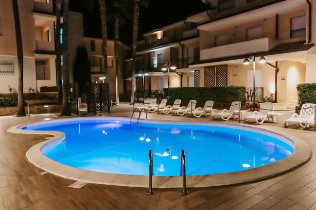 Piscina illuminata di notte, circondata da lettini.