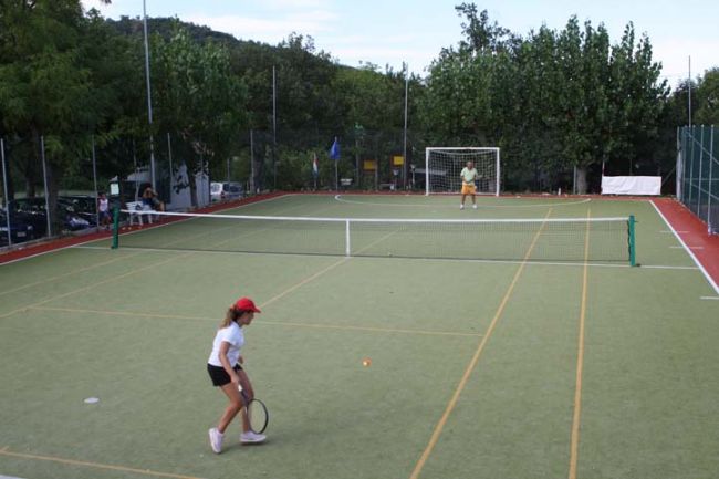 Ragazza con cappellino rosso gioca a tennis su un campo all'aperto.