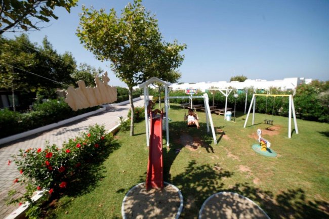 Parco giochi con altalene e scivolo su prato verde.
