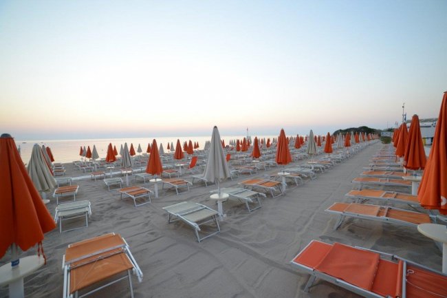 Spiaggia con file di lettini e ombrelloni arancioni.