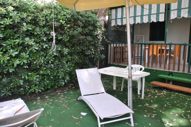 Un patio con sdraio, ombrellone e tavolo bianco.