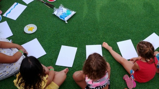 Bambini seduti sull'erba con fogli bianchi per dipingere.