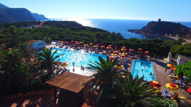 Vista di una piscina con ombrelloni rossi e gialli e il mare sullo sfondo.