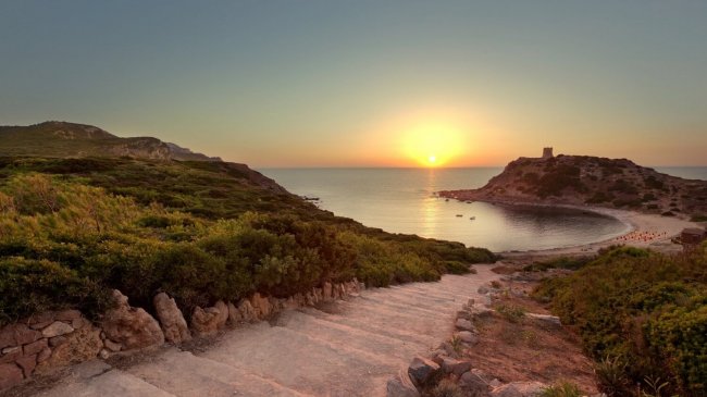 Sentiero costiero al tramonto con vista sul mare e promontorio.