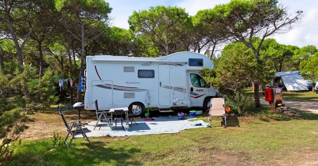 Camper bianco parcheggiato su erba con sedie all'esterno.