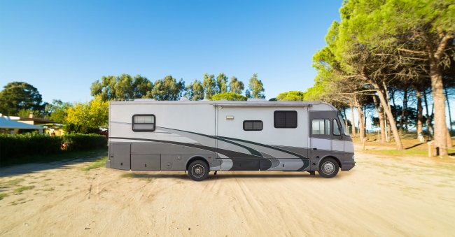 Camper parcheggiato su terreno sabbioso vicino a pini.