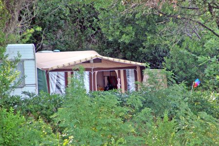 Una roulotte e una tenda nel mezzo della vegetazione.