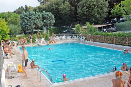 Piscina con persone che nuotano e altre sedute a bordo vasca.