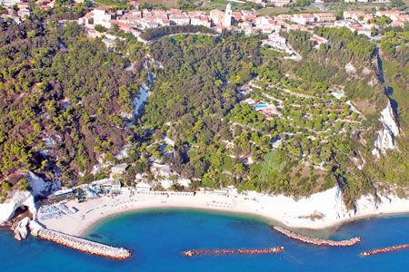 Vista aerea di una spiaggia sabbiosa con acque blu e un paese su una collina verde.