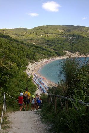Sentiero verso una spiaggia con persone, collina e mare.