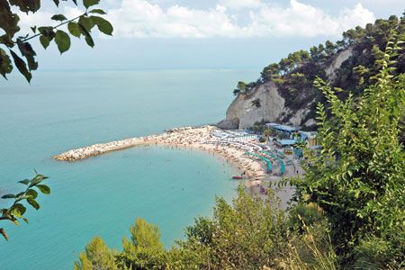 Spiaggia affollata con mare turchese e colline verdi.