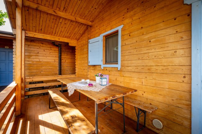 Veranda in legno con tavolo, panche e finestre azzurre.