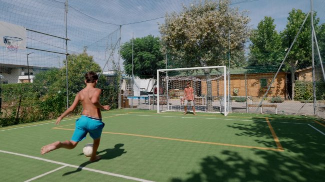Ragazzo calcia un pallone verso la porta in un campetto.