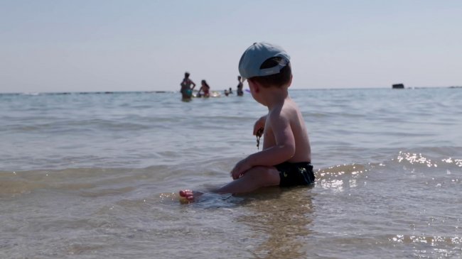 Bambino seduto in acqua bassa al mare.