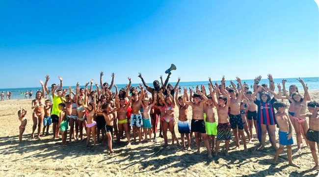Grande gruppo di bambini sulla spiaggia con le mani alzate.