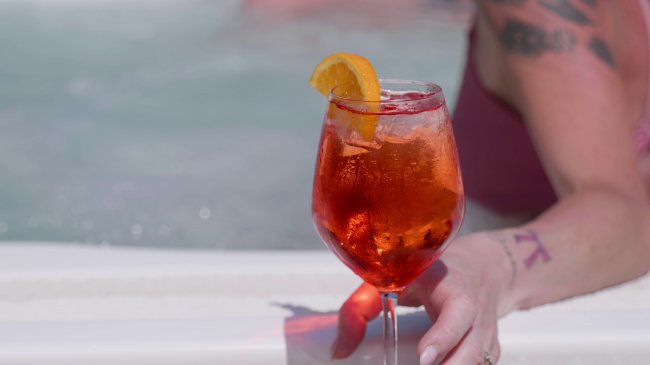 Mano con cocktail arancione in piscina.