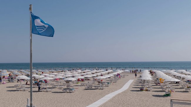 Spiaggia con ombrelloni bianchi e bandiera blu.