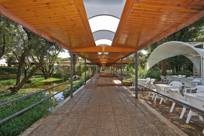 Passaggio coperto in legno con tavoli e sedie bianche accanto a un giardino.