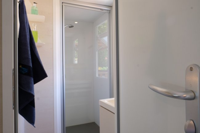 Bagno moderno con doccia, asciugamano blu appeso e mensole con prodotti.