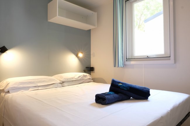 Letto matrimoniale con asciugamani blu, luce da parete accesa.