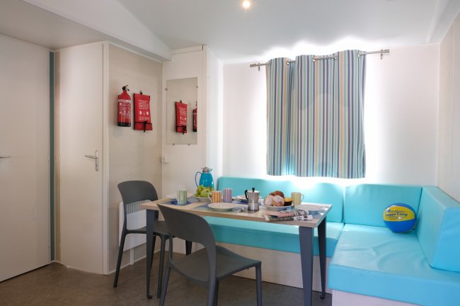 Sala da pranzo con sedie grigie, tavolo apparecchiato, divanetto blu e tendine rigate.