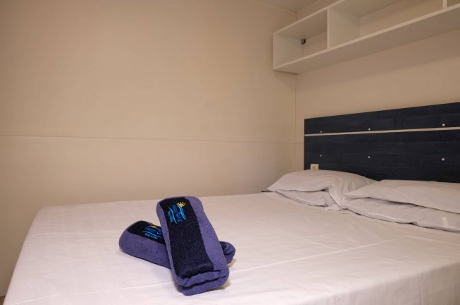 Letto matrimoniale con asciugamani piegati sopra, interni minimalisti.