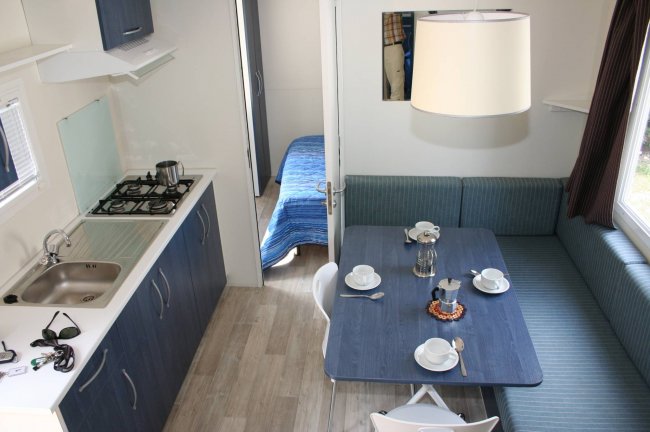 Una cucina moderna con tavolo apparecchiato, lavello e fornello a gas vicino a un piccolo soggiorno.
