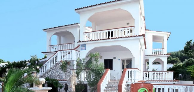 Villa bianca a tre livelli con balconi, scale e piante.