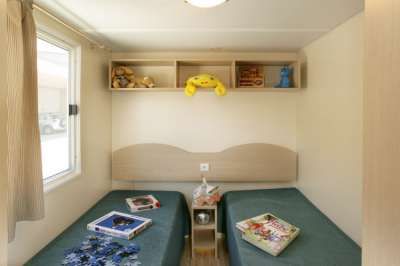 Camera con due letti singoli, libri e peluche sugli scaffali.