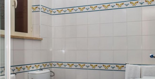 Bagno con piastrelle bianche, decorazioni blu e gialle, e finestra accanto a un bidet.