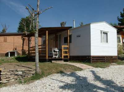 Una casa mobile bianca con veranda in legno e sedia.