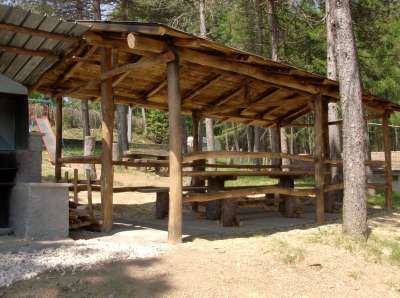 Tavoli da picnic sotto una tettoia di legno in un'area boschiva.