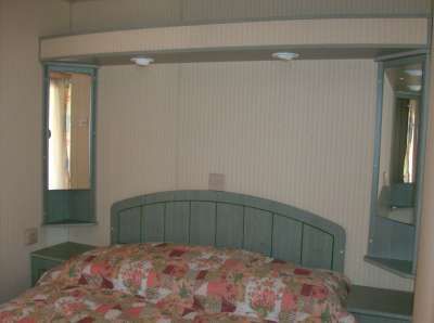 Una testiera curva di legno verde con specchi laterali sopra un letto con copriletto patchwork.