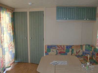 Soggiorno di una casa mobile con tavolo, divano colorato e pensili verdi.