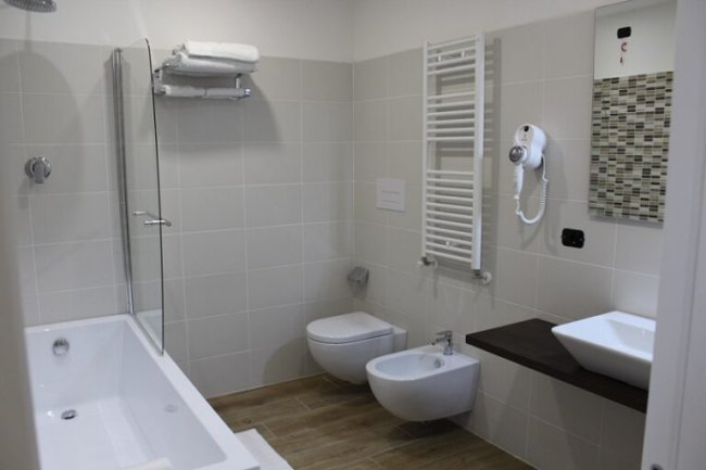 Bagno con vasca, sanitari moderni, rivestimenti chiari e un asciugacapelli a parete.