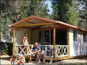 Una famiglia seduta davanti a una casetta con veranda in un ambiente alberato.
