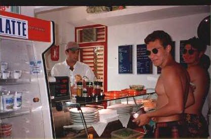 Due uomini in una gelateria, uno in costume da bagno. Frigorifero con latte sulla sinistra.