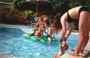 Piscina con adulti e bambini che giocano con un materassino gonfiabile.