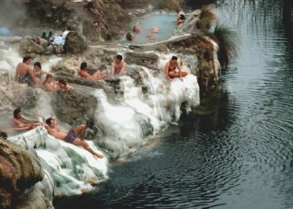 Persone rilassate in vasche termali naturali vicino a un lago.