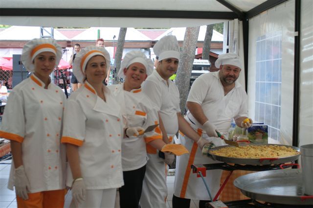 Un gruppo di cuochi in divisa bianca e arancione vicino a una grande padella.