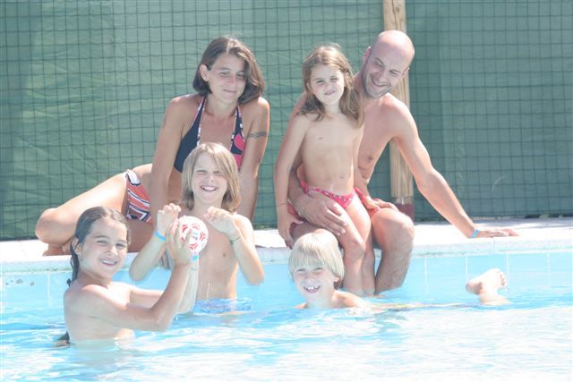 Gruppo di persone sorridenti in una piscina, con alcuni che giocano con una palla.
