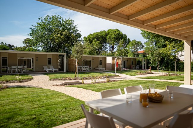 Patio coperto con tavolo e sedie, giardino e vialetti curati.
