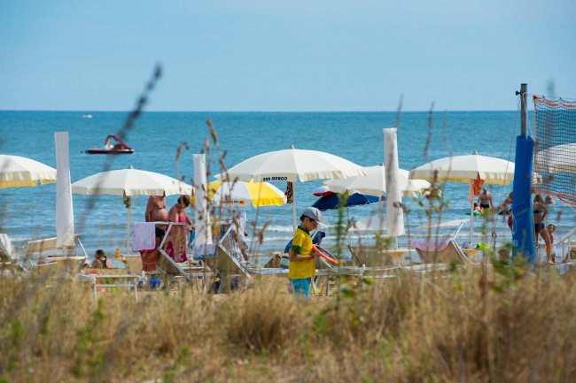 Spiaggia con ombrelloni bianchi e gente in riva al mare.