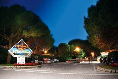 Entrata di un campeggio di notte, con un grande cartello illuminato e alberi intorno.