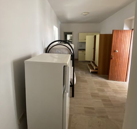 Corridoio con frigorifero, letti a castello e porta d'ingresso aperta.